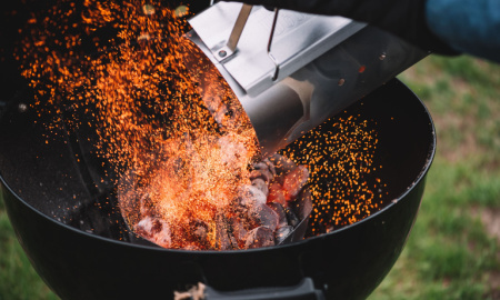 Fire sparks caught up in the moment of putting hot wood charcoal from the fire starter into the weber GBS charcoal barbecue grill, close up view