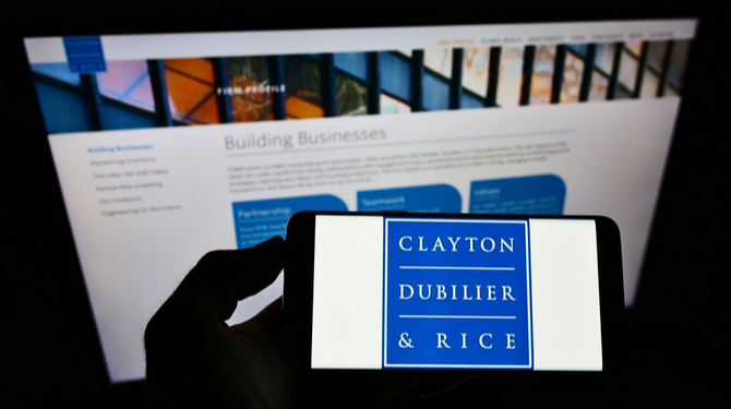 Person holding smartphone with logo of US private equity firm Clayton, Dubilier and Rice LLC on screen in front of website. Focus on phone display. Unmodified photo.